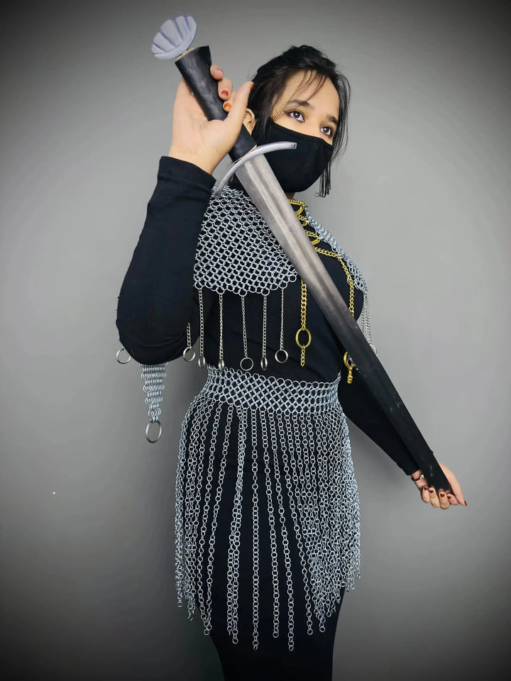 Person wearing a chainmail skirt and holding a sword against a gray background