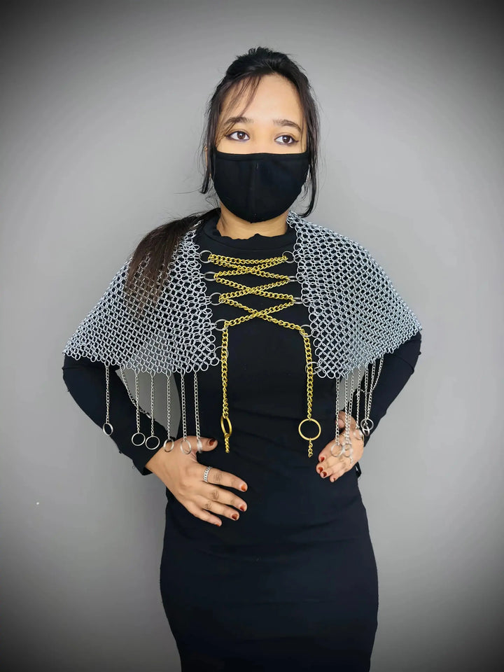 Person wearing a black outfit with a chainmail shawl and black mask against a gray background