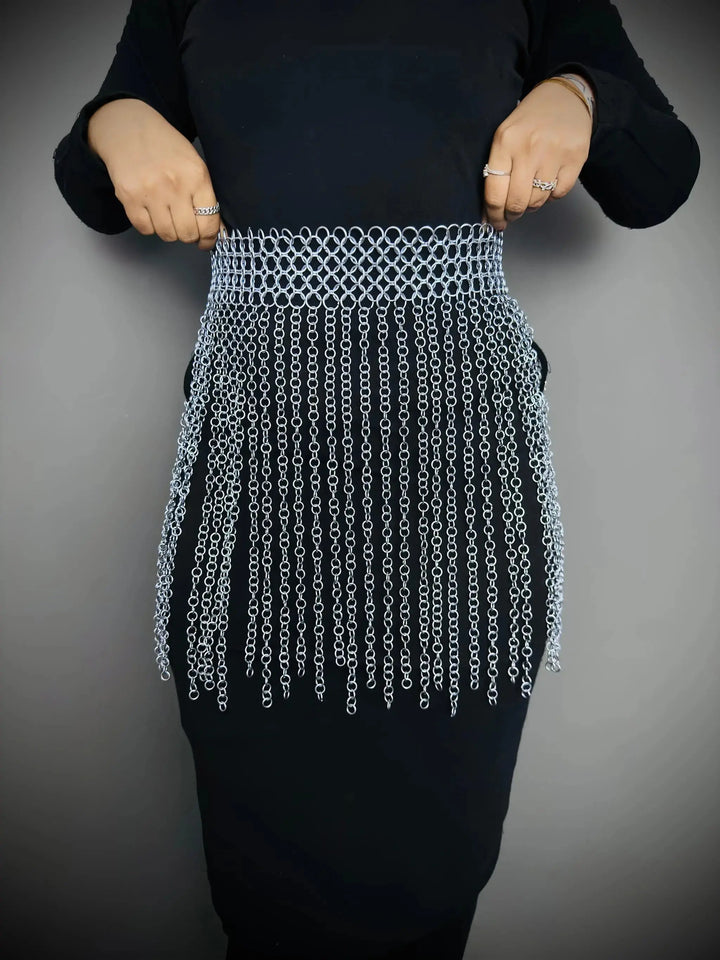 Person wearing a black top and a unique chain-patterned skirt on a gray background