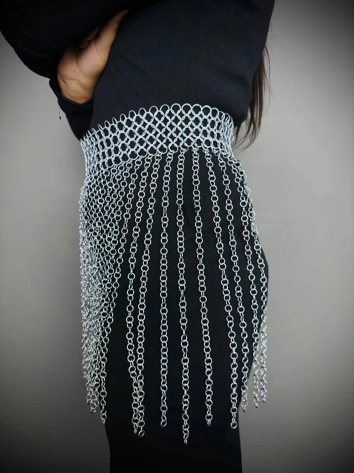 Person wearing a black outfit with a silver chain fringe detail on a plain background