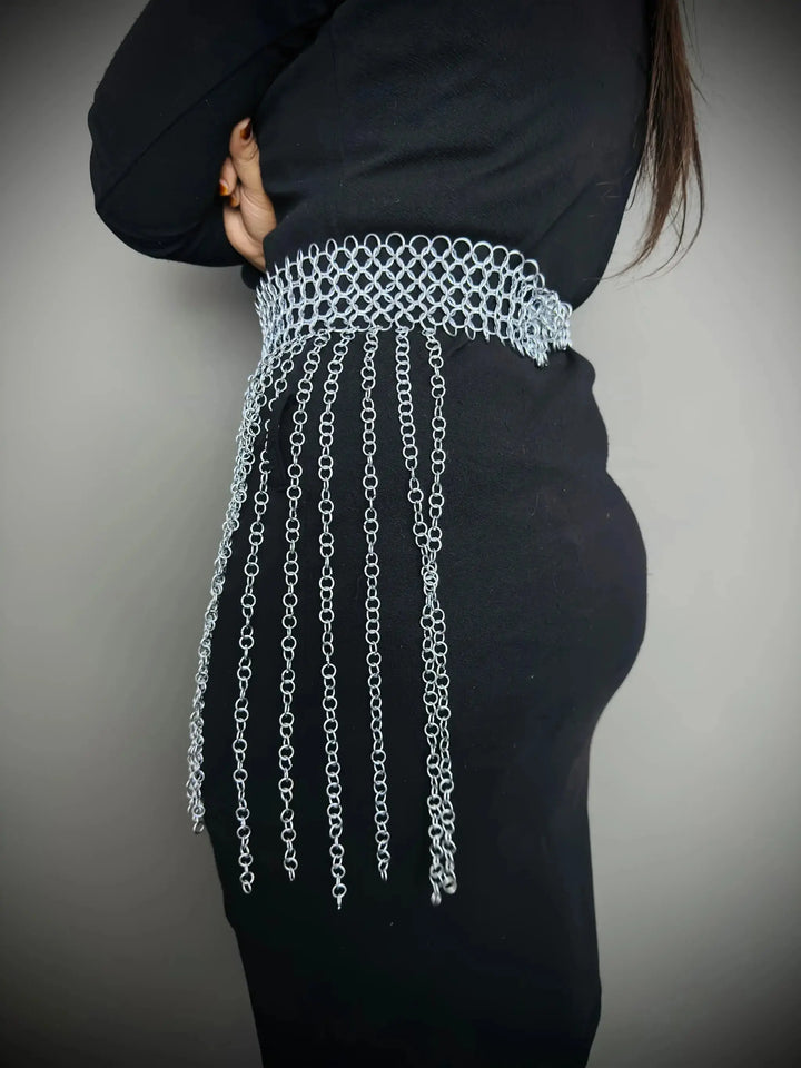 Person wearing a black outfit with a silver chain detail on a plain background